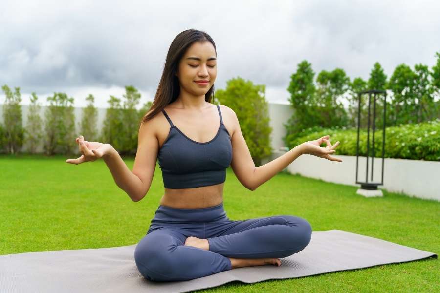 Une jeune femme médite en plein air, illustrant le lien positif entre le yoga et santé mentale.