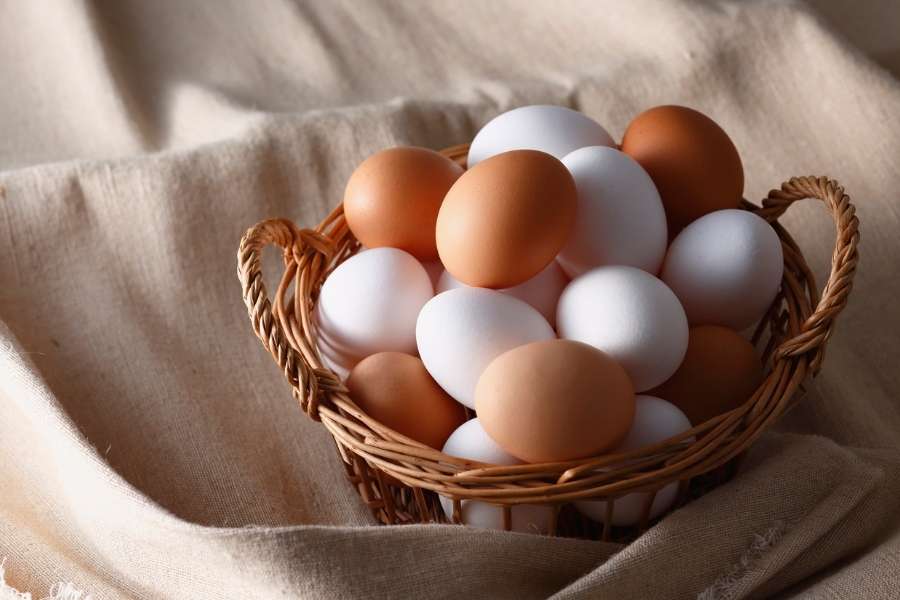 Un panier en osier rempli d'œufs frais blancs et bruns, posé sur un tissu de lin beige.