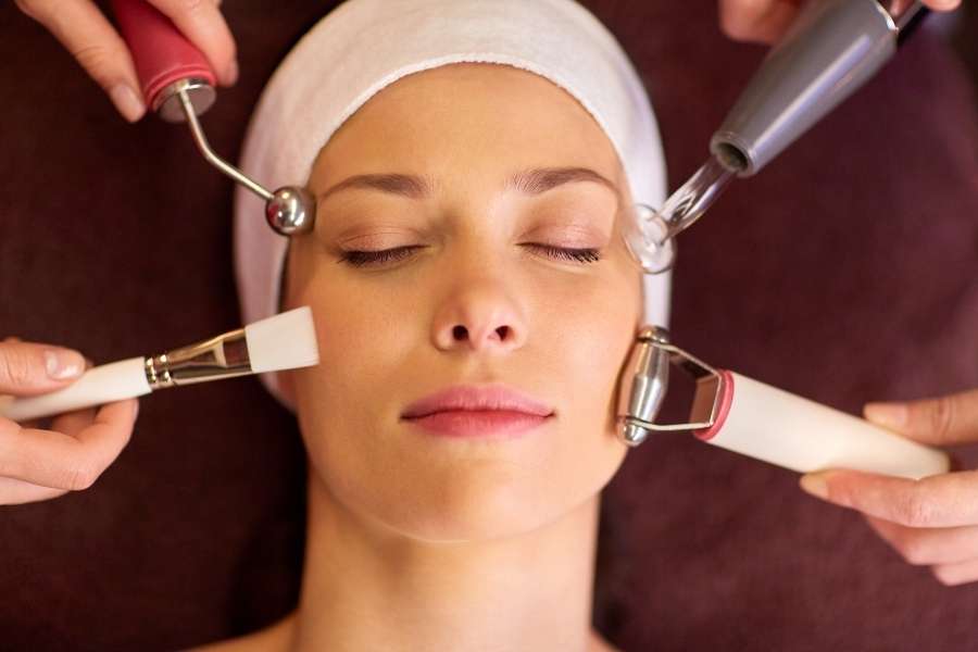Une femme reçoit des soins du visage high-tech avec plusieurs outils esthétiques sur sa peau.